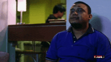 a man in a blue shirt is sitting in front of a sign that says " bul "