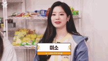 a woman wearing a blue jacket and a yellow shirt is sitting in front of a shelf of snacks .