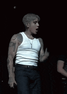 a man wearing a white tank top and black pants has a tattoo on his arm