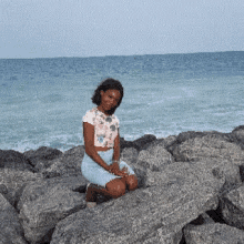 a young girl sits on a rock near the ocean