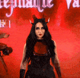 a woman in a devil costume with horns stands in front of a sign that says ' agatha ' on it