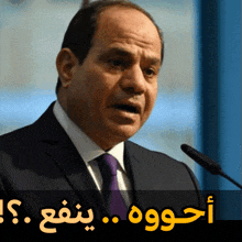 a man in a suit and tie speaking into a microphone with arabic writing behind him