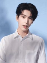 a young man wearing a white shirt is standing in front of a blue wall