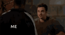 a man in a black jacket is talking to another man in a living room while making a funny face .