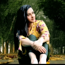 a woman in a yellow floral shirt is sitting in a forest