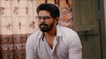 a man with glasses and a beard is sitting in front of a green door