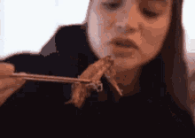 a woman eating a piece of meat with chopsticks