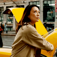 a woman in a trench coat leans on a yellow taxi