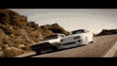 two cars are driving down a road with a hill in the background