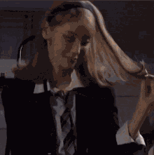 a woman wearing a suit and tie is holding her hair .