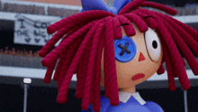 a stuffed doll with red dreadlocks and a blue button in her eye