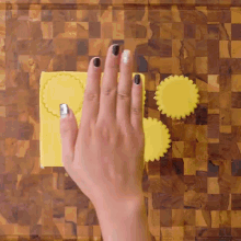 a woman 's hand with black nail polish is holding a piece of yellow clay