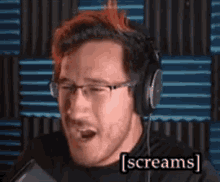 a man wearing headphones and glasses is screaming into a microphone and says screams .