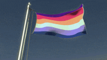 a rainbow flag flies in the wind against a blue sky