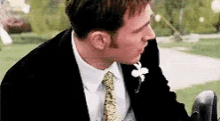 a man in a suit and tie is sitting in a chair and talking on a cell phone .