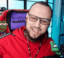 a man wearing glasses and a red shirt is sitting in front of a twitch screen