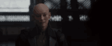 a bald man in a black jacket is sitting in a dark room .