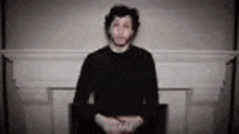 a man in a black shirt is standing in front of a fireplace in a room .