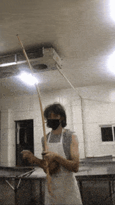 a man wearing a mask is holding a long wooden stick in a kitchen