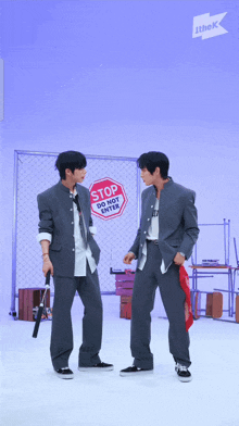 two men standing next to each other in front of a fence with a stop sign on it