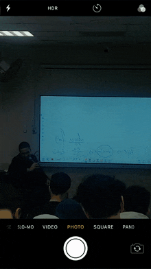 a phone screen shows a man in front of a white board with the word hdr visible