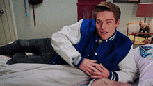 a young man wearing a blue and white varsity jacket laying on a bed