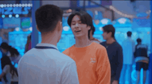a man in an orange shirt is talking to another man in a white shirt in an arcade .
