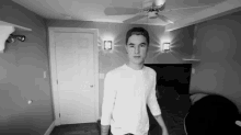 a man in a white shirt is standing in a room with a ceiling fan