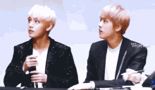 two young men are sitting next to each other at a table and looking at each other .