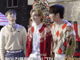 three young men are standing in front of a christmas tree and one of them has the letter k on his sweater