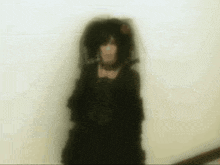 a woman in a black dress and veil is standing in front of a white wall