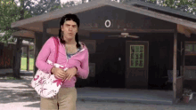 a man in a pink jacket stands in front of a house with the number 0 on the front