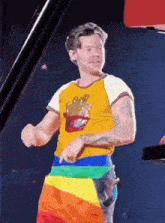 a man in a yellow shirt and rainbow shorts is dancing on a stage