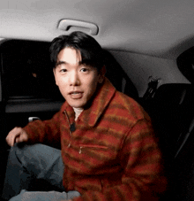a man is sitting in the back seat of a car wearing a plaid jacket