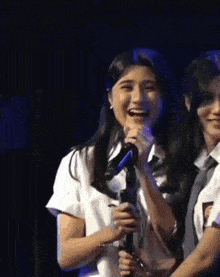 a girl is holding a microphone and laughing while standing next to another girl .