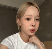 a young woman with blonde hair is wearing a white shirt and looking at the camera .