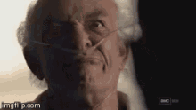 an older man wearing an oxygen mask is looking at the camera .