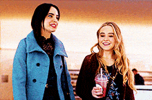 two women are standing next to each other and one is holding a smoothie .