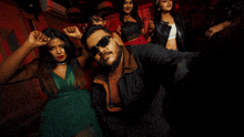 a man wearing sunglasses takes a selfie with a group of women dancing in the background