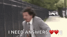 a man in a suit and tie is running down a street and saying i need answers .
