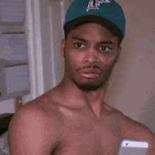 a man without a shirt is wearing a blue hat and making a face .
