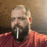 a man with a beard is smoking a cigarette while wearing a red shirt