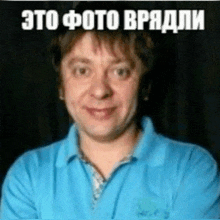a man in a blue shirt is smiling with his arms crossed in front of a black background with russian writing on it .