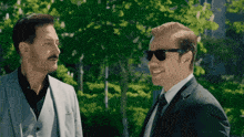 two men in suits and sunglasses are standing next to each other and smiling