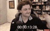 a man is sitting in front of a microphone in a room with a clock that says 00 : 00.13 .