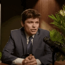 a man in a suit and tie is talking into a microphone while holding a coffee mug with the letter af on it .