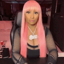 a woman with pink hair is sitting at a desk wearing a necklace .
