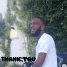a man with a beard is standing in front of trees and says thank you
