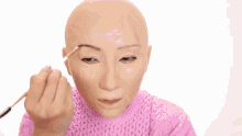 a woman wearing a pink sweater is holding a makeup brush and a powder