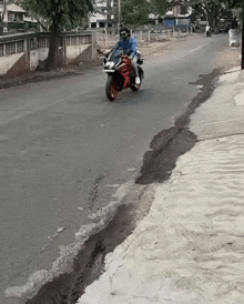 a man is riding a red motorcycle down a street next to a sidewalk .